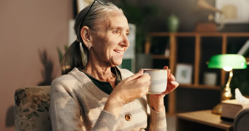 An elderly woman at home drinking tea months after recovering from shoulder replacement surgery