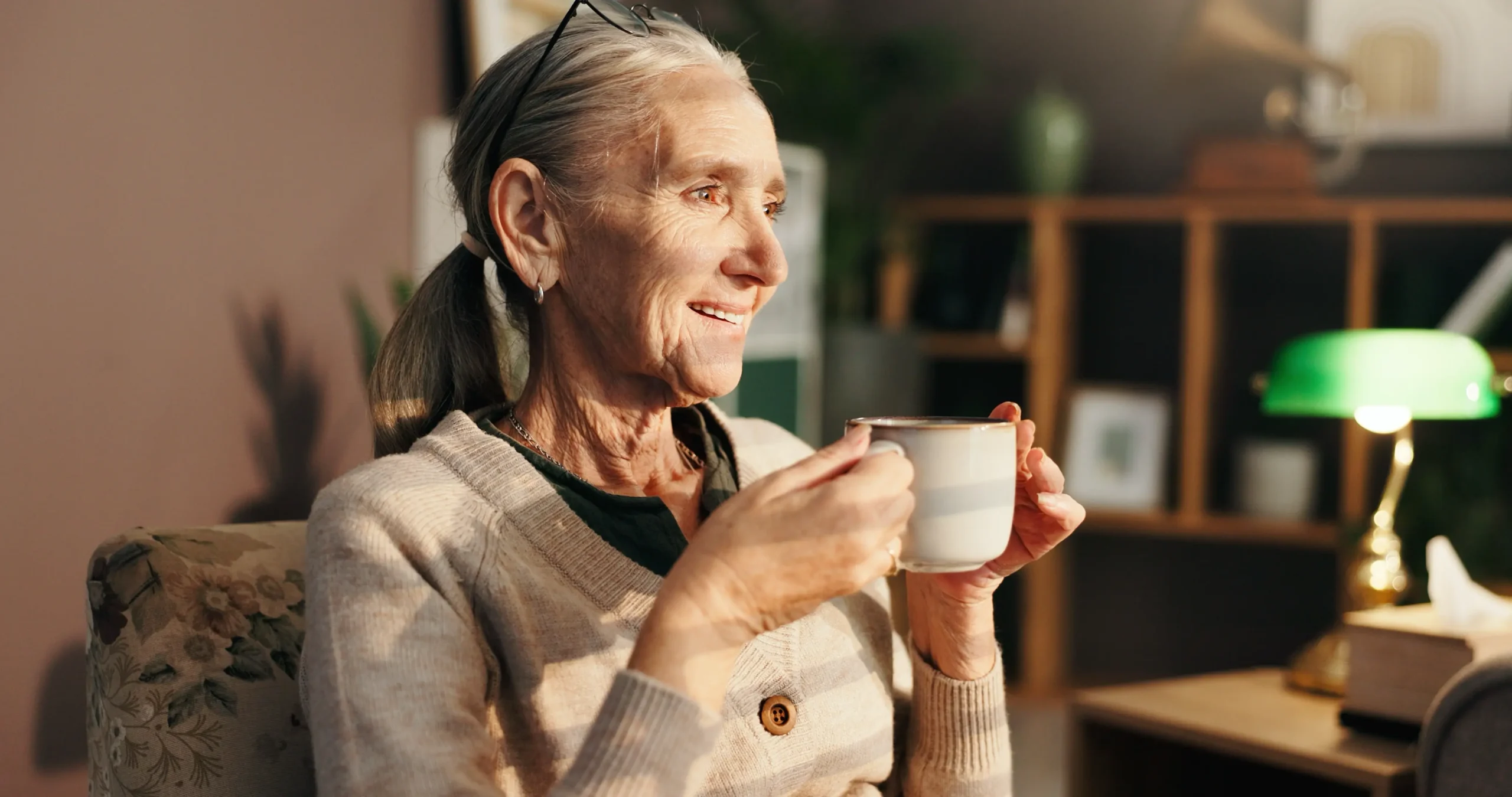 An elderly woman at home drinking tea months after recovering from shoulder replacement surgery