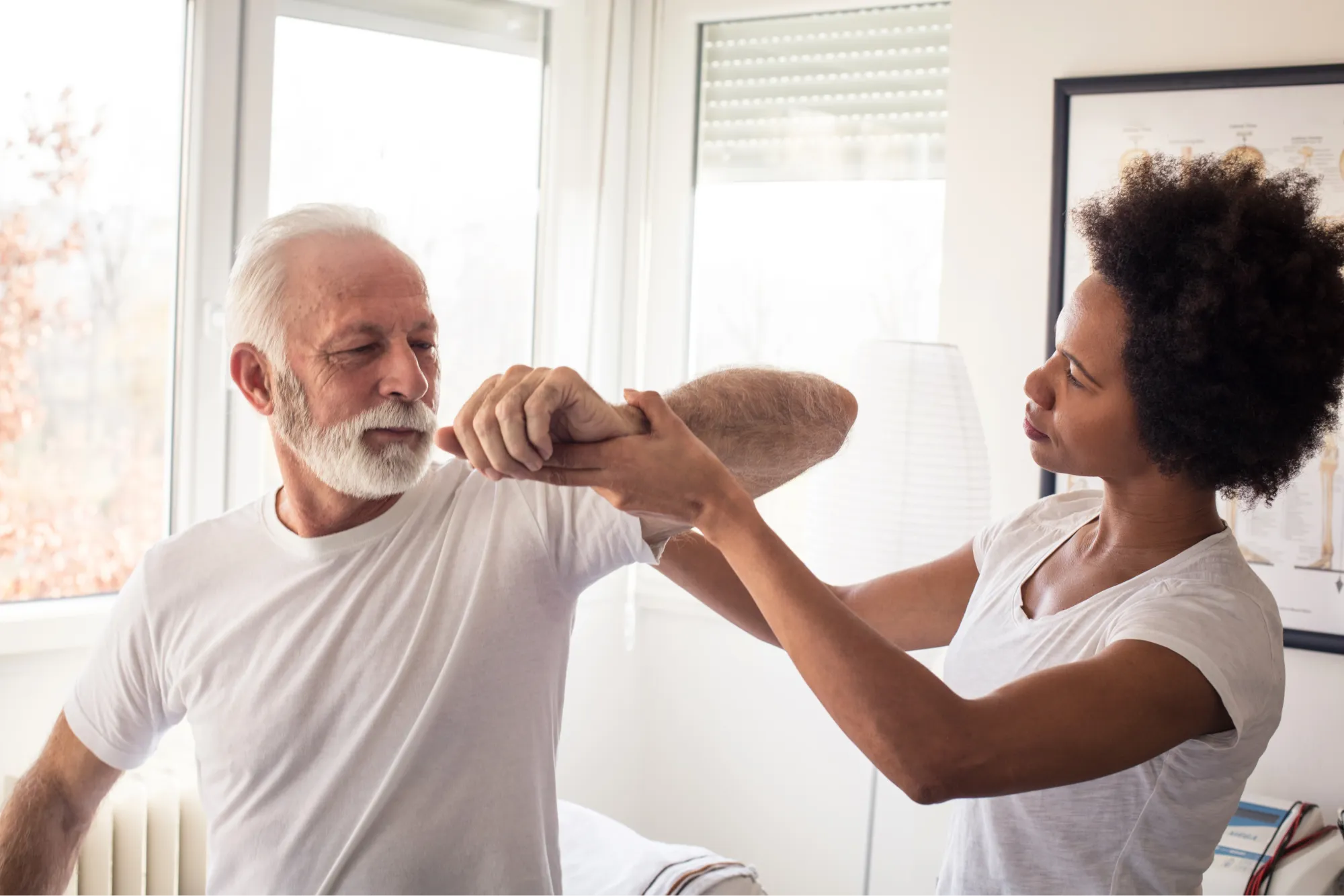 Physical therapist guiding a senior man through a shoulder range-of-motion exercise during recovery.